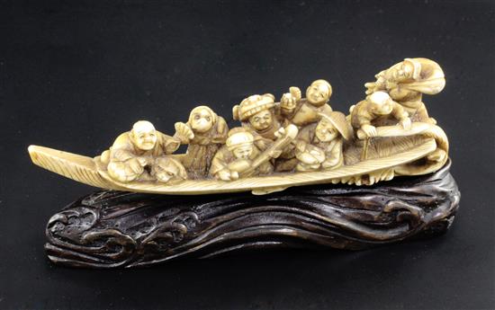 A Japanese ivory okimono of figures enjoying festivities on a boat, Meiji period, 12.3cm, wood stand